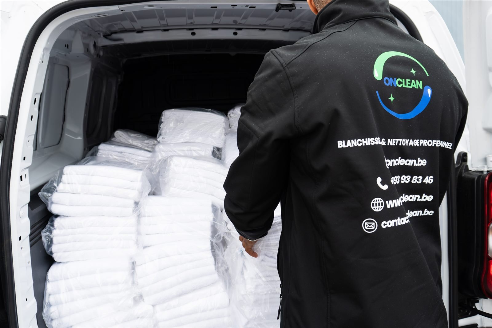 Livreur OnClean devant des piles de linge blanc